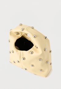 Μαλακή κίτρινη τσάντα χειρός με συγκεντρωμένη λαβή, διακοσμημένη με λαμπερά ασημένια καρφάκια τοποθετημένα ομοιόμορφα, που εμφανίζει εσωτερική τσέπη με φερμουάρ σε σκούρο χρώμα.