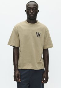 T-shirt khaki a maniche corte in cotone, con un logo marrone scuro sul petto, dalla vestibilità comoda e colletto rotondo. Design semplice e monocolore.