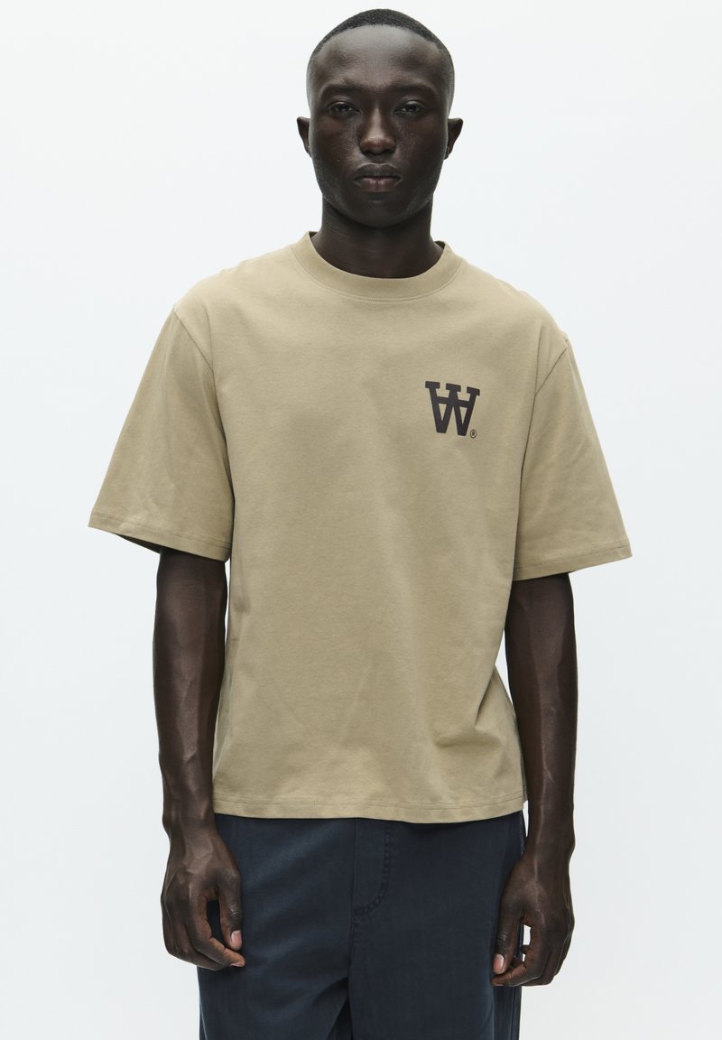 T-shirt khaki a maniche corte in cotone, con un logo marrone scuro sul petto, dalla vestibilità comoda e colletto rotondo. Design semplice e monocolore.