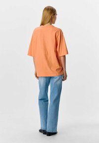 Camiseta de algodón naranja de manga corta, de corte relajado y cuello redondo, combinada con unos vaqueros rectos azul claro y zapatos negros.