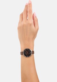 Bruin leren horloge met een ronde, zwarte wijzerplaat met grote witte cijfers op 3, 6, 9 en 12, zilverkleurige metalen accenten.