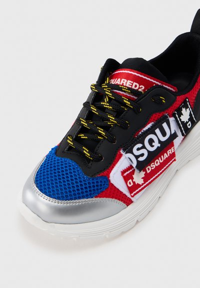 Πολύχρωμο αθλητικό παπούτσι με κόκκινο δίχτυ, μπλε λεπτομέρειες, μαύρα κορδόνια και ασημένιες λεπτομέρειες. Περιλαμβάνει ετικέτες με λογότυπα και υφασμάτινες υφές.