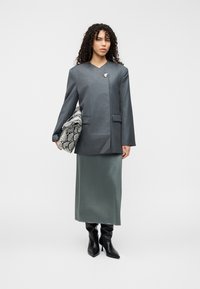 Γκρι υπερμεγέθη σακάκι με V-λαιμόκοψη, σε συνδυασμό με μακριά πράσινη σατέν φούστα, μαύρα στιλάτα μπότες έως το γόνατο και τσαντάκι με σχέδιο φιδιού.