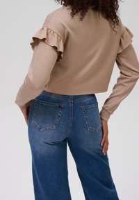 Top corto beige con mangas acampanadas combinado con jeans azules de cintura alta con bolsillos y un lavado degradado de claro a oscuro.