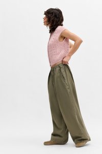 Top sin mangas de punto rosa con un patrón texturizado, combinado con pantalones holgados de color verde oliva que tienen una cintura elástica y bolsillos laterales.