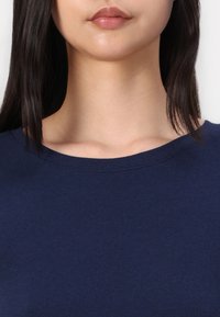 Tamno plavi pamučni majica s okruglim izrezom i kratkim rukavima. Mekana tekstura, minimalni šavovi oko ovratnika.