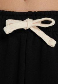 Pantaloni della tuta neri con una cintura in vita testurizzata e un cordoncino in cotone color avorio annodato a fiocco sul davanti.