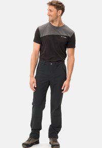 Camicetta nera e grigia a maniche corte con design a blocchi di colore orizzontali, abbinata a pantaloni neri con zip e una vestibilità comoda.