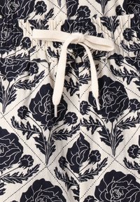 Bomulds shorts med elastisk talje, prydet med et blomsterdesign i navy blå på en cremet baggrund, samt en snørebåndssløjfe med metalspidser.