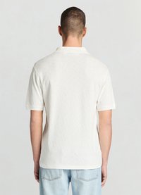 Polo blanc à manches courtes avec un motif en diamant texturé et un col classique, doté d'une coupe décontractée et d'un ourlet.