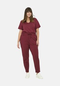 Bordeaux, T-shirt met korte mouwen, ontspannen pasvorm, gecombineerd met bijpassende taps toelopende broek met een trekkoord in de taille. Model draagt witte sneakers.