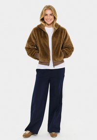 Hnědá umělá kožešinová zkrácená bunda s kapucí, se zipem a žebrovanými manžetami, spárovaná s bílou košilí a námořnickými širokými kalhotami.