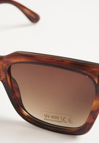 Schildpatt-Sonnenbrille mit braunen Verlaufslinsen, rechteckiger Form und UV 400-Schutzlabel. Dezenter, glänzender Finish.