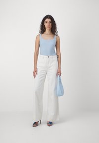Débardeur à rayures bleu clair, pantalons blancs à jambes larges, sac à main bleu et talons strappés bleus, mettant l'accent sur des formes épurées et des couleurs contrastées.