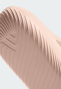 Semelle d'une sandale glissante rose clair avec des rainures incurvées et un logo à trois bandes en relief près du talon.