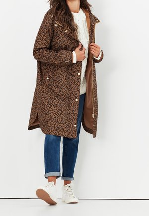 Abrigo largo de estampado de leopardo marrón con cierre de cremallera y broches a presión, con forro suave y dos bolsillos laterales, combinado con jeans azules remangados y zapatillas blancas.