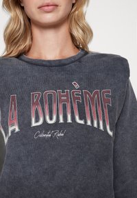 Ciemnoszara bluza z okrągłym dekoltem, z napisem "LA BOHÈME" w czerwonym gradiencie oraz "Colorful Rebel" wyszytym poniżej. Miękka tekstura.