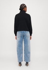 Maglione a collo alto a maglia nera abbinato a jeans a gamba larga di un blu chiaro con un motivo sbiadito e scarpe nere con tacco alto.