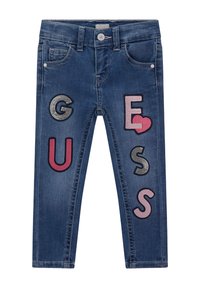 Blue denim jeans featuring colorful embroidered letters and symbols: "G", "U", "E", "S", with a heart motif and textured accents.