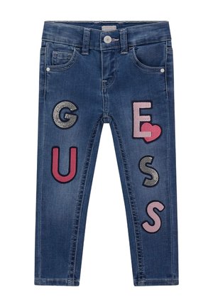 Modre jeans iz denima z barvitimi vezenimi črkami in simboli: "G", "U", "E", "S", s srčnim motivom in teksturiranimi akcenti.