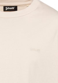 T-shirt di cotone color crema con scollatura rotonda, caratterizzato da un logo in rilievo discreto sulla zona del petto e una texture morbida e liscia.