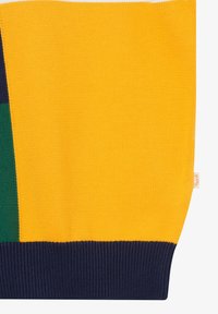 Tissu tricoté avec des blocs de couleur jaune, bleu marine et vert foncé, comportant une petite étiquette beige sur le bord.