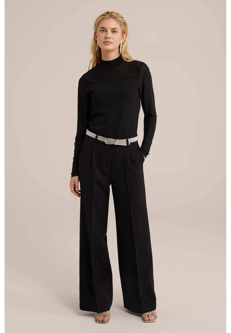 Zwarte, aansluitende langemouwen top met een hoge kraag, gecombineerd met wijde zwarte broeken en een riem met zilveren accenten. Gelaagd stof.