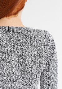 Svart och vit texturerad tyg med ett vävt mönster. Har en hög halsringning och en liten dragkedjefetajl i ryggen.