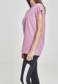 Camiseta de algodón rosa con mangas cortas, con un ajuste relajado. Combinada con leggings negros que tienen un detalle de banda lateral blanca.