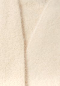 Tejido de color crema con una textura suave y peluda y un patrón sutil, que presenta dos piezas superpuestas en un ángulo, mostrando su calidad ligera.