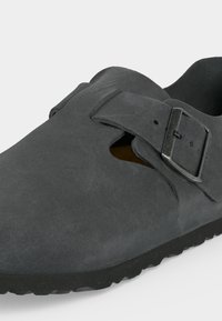 Σκούρο γκρι παπούτσι τύπου slip-on με ρυθμιζόμενο μεταλλικό λουράκι και λαστιχένια σόλα, με ομαλή υφή σουέντ και ανοιχτό πλαϊνό άνοιγμα.