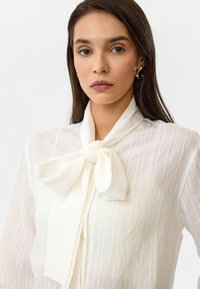 Witte blouse met een strikkraag, verticale gestreepte textuur, lange mouwen en doorzichtig stof. Soepel, lichtgewicht materiaal.