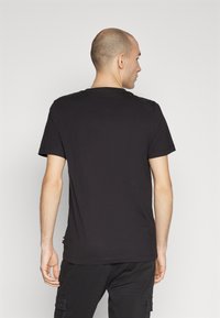 T-shirt nera a maniche corte con collo rotondo. Realizzata in cotone, presenta un piccolo etichetta logo all'orlo laterale. Design semplice.