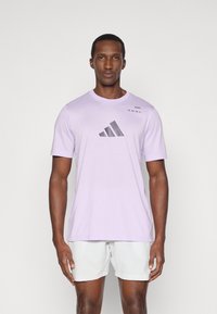 Jasnofioletowa koszulka bawełniana z czarnym logo Adidas i napisem na górnej lewej stronie. Krótkie rękawy i klasyczny dekolt.