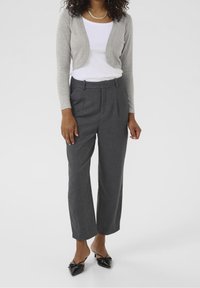 Cárdigan gris corto, blusa blanca, pantalones grises con pliegues y zapatos negros de punta. Texturas suaves con un diseño minimalista.