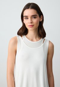 Top bianco senza maniche con scollatura rotonda e dettagli a strati, realizzato in tessuto morbido e caratterizzato da una texture liscia.