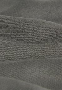 Ciemnoszary materiał o miękkiej fakturze, ukazujący lekko nierówny wzór i subtelne szczegóły tkaniny, złożony tak, aby tworzyć delikatne fałdy.