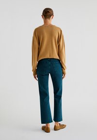 Camelinvärdtröja med sänkt axel, i kombination med mörk teal vida jeans. Noterbara leopardmönstrade lägenheter kompletterar outfiten.