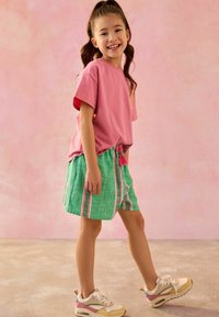 T-shirt rose à manches courtes et shorts rayés verts avec cordon de serrage. L'enfant porte des baskets multicolores avec une finition texturée.