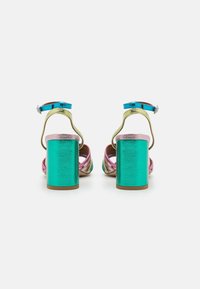 Sandali con tacco a spillo dotati di un tacco a blocco metallico turchese, cinturino alla caviglia blu regolabile e tomaia multicolore iridescente nei toni rosa e oro.