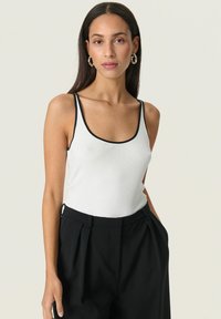 Weißes, geripptes Tanktop mit schwarzem Saum, schmalen Trägern und einem runden Halsausschnitt, kombiniert mit hochgeschnittenen schwarzen Hosen.
