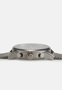 Montre en acier inoxydable avec un bracelet en maille grise, cadran noir rond, marqueurs d'heure argentés et deux boutons latéraux ; logo de la marque sur la couronne.