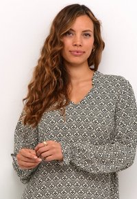 Dlhý rukáv blúzky v krémovej farbe s čiernym ozdobným kvetinovým vzorom, so V-výstrihom a naťahovacími manžetami. Hladká, ľahká tkanina.