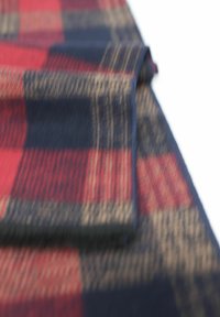 Tissu à carreaux rouges et marins avec une texture douce, présentant de grands carrés et des accents beiges, plié sur le bord.