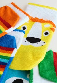 Chaussettes colorées avec divers motifs : un visage de lion jaune, des rayures bleues et des designs verts. Material en tricot doux avec des teintes vives.