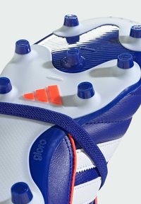 Zapato de fútbol azul con un upper texturizado, rayas blancas y un acento naranja. Suela con tachuelas, que combina tachuelas circulares y cónicas.
