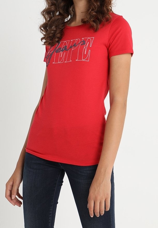 Mujer con una camiseta roja ajustada que tiene el logotipo "PEPE" en texto blanco y azul marino contorneado, combinada con jeans azul oscuro, contra un fondo blanco.