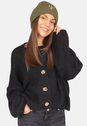 Black knitted cardigan with loose sleeves and three gold-tone buttons, paired with a green ribbed beanie featuring a brown accent.
