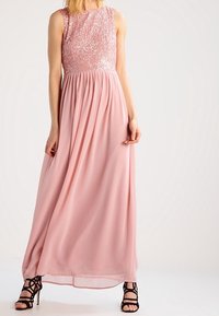 Rosa maxiklänning med en paljett-dekorerad liv och en flödande chiffongkjol. Har en rund halsringning och svarta klacksandaler med remmar.