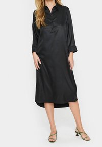 Svart satin skjortklänning med krage, knappfront, trekvartsärmar och en lätt rundad fåll. Matchad med gröna remsandaler.